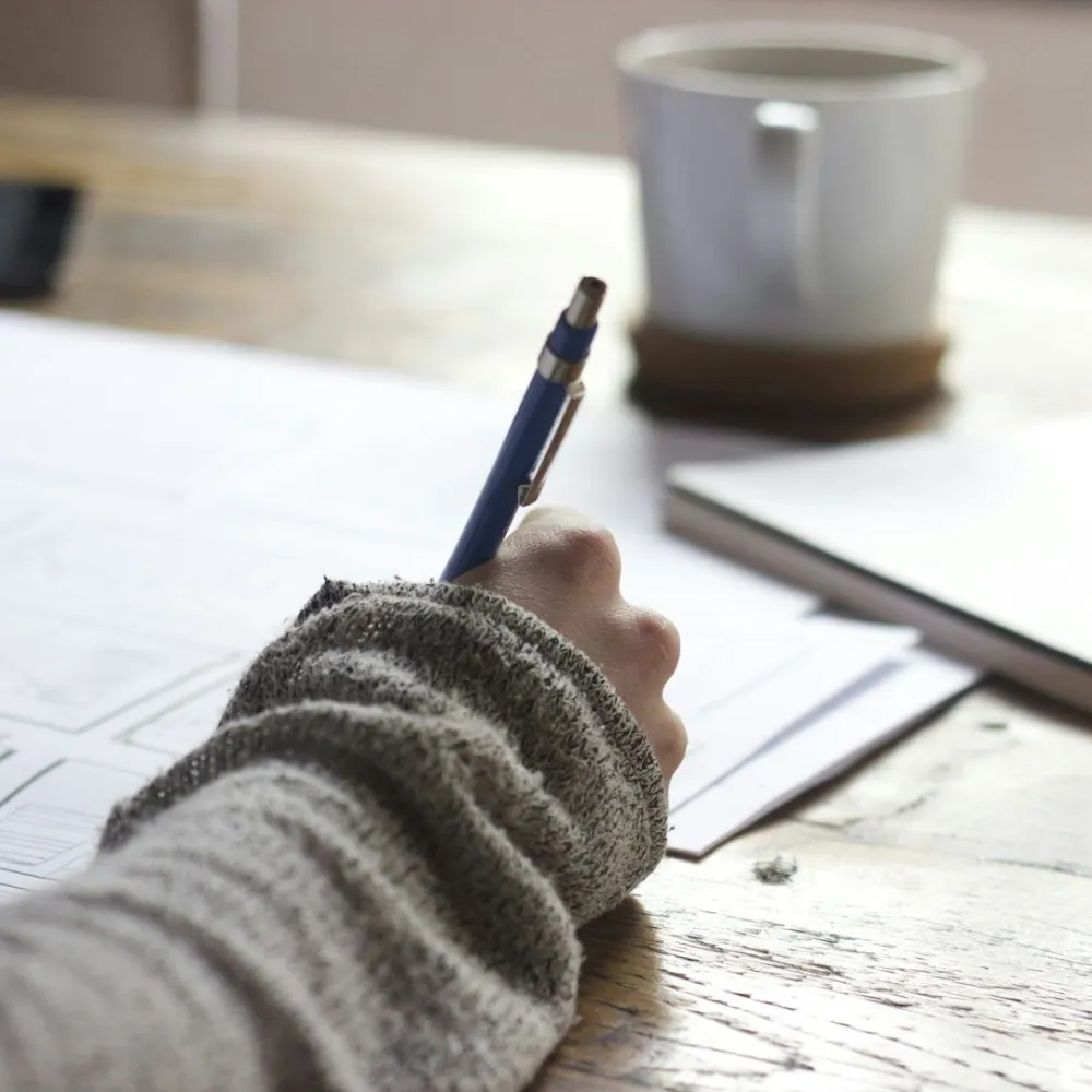 Hand sketching on technical drawings beside a cup of coffee